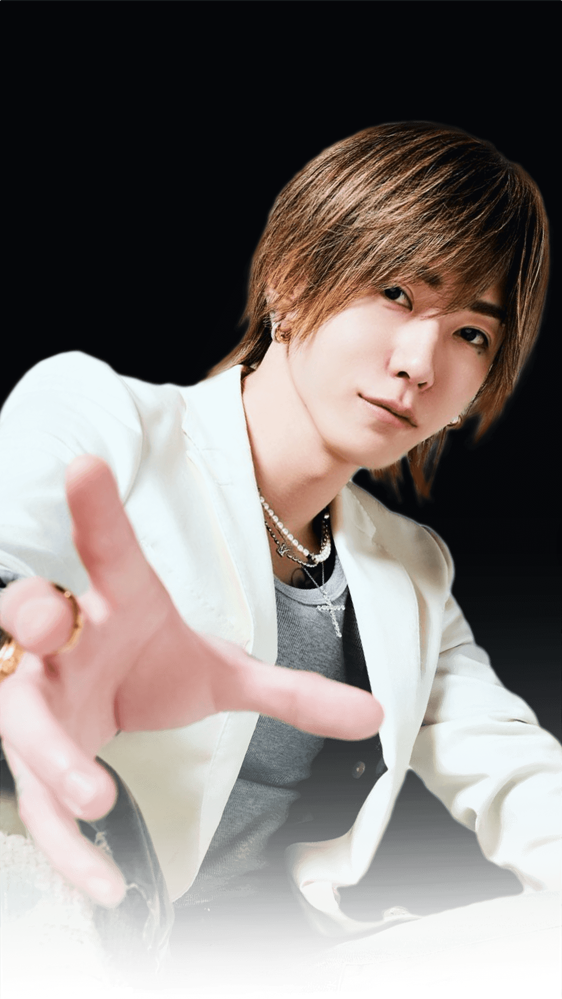 黒い背景で腕を組み見つめるおじゃる丸社長。ファッション性の高いタトゥーとアクセサリーが印象的なポートレート写真。